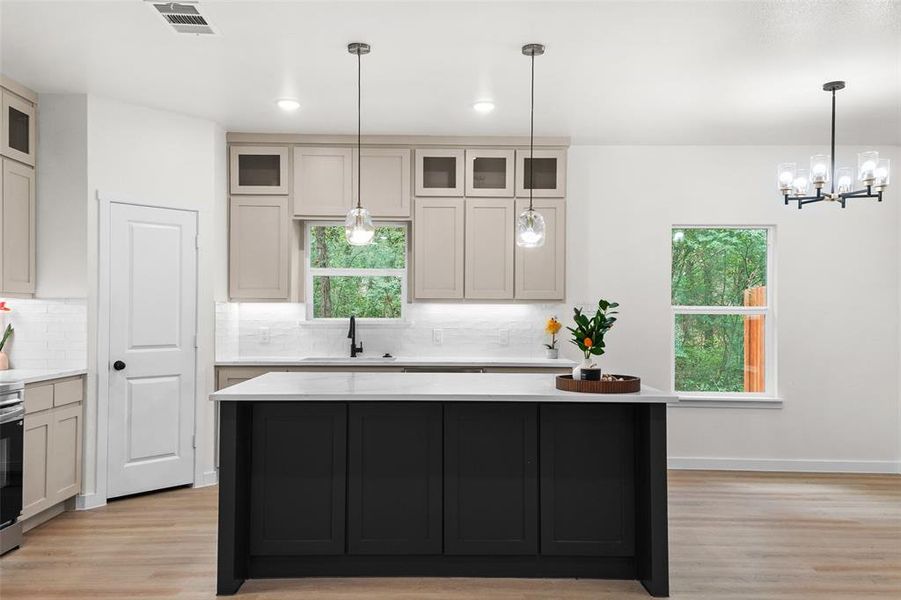 Modern kitchen featuring a central island with a light-toned countertop, a matte black kitchen faucet, light wood-finish flooring, and pendant lighting fixtures Modern kitchen featuring a central island with a light-toned countertop, a matte black kitchen faucet, light wood-finish flooring, and pendant lighting fixtures