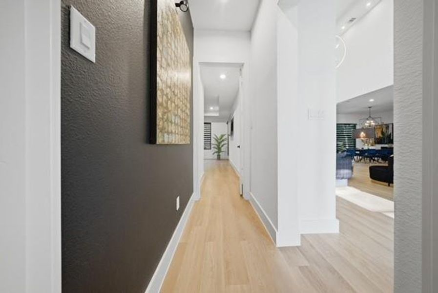 Bright hallway featuring light wood-finish flooring, white baseboards, and a contrasting dark accent wall
