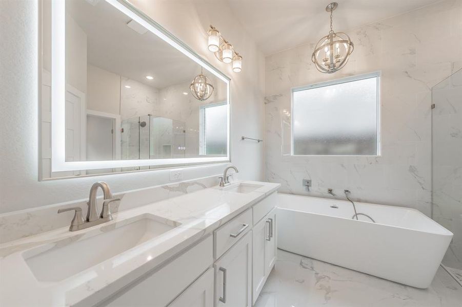 Full bath with light marble finish floors, double vanity, a freestanding bath, a marble finish shower, and a chandelier