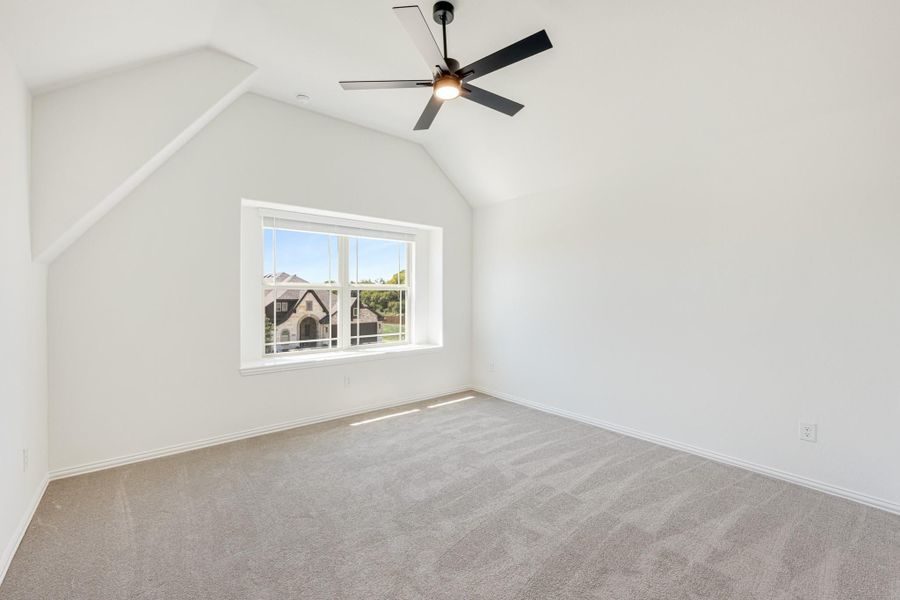 Empty bedroom with vaulted ceiling, ceiling fan, carpet flooring, and a window with neighborhood view Empty bedroom with vaulted ceiling, ceiling fan, carpet flooring, and a window with neighborhood view