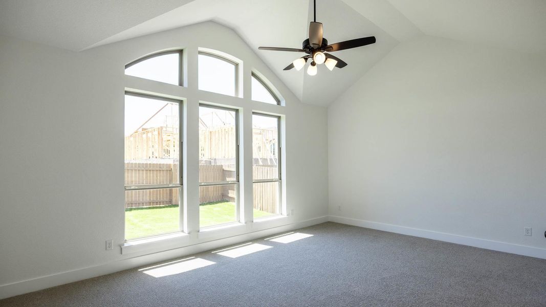 Carpeted empty room with a wealth of natural light, ceiling fan, vaulted ceiling, and baseboards Carpeted empty room with a wealth of natural light, ceiling fan, vaulted ceiling, and baseboards