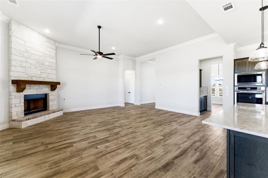 Unfurnished living room with crown molding, a stone fireplace, light wood-type flooring, ceiling fan, and recessed lighting