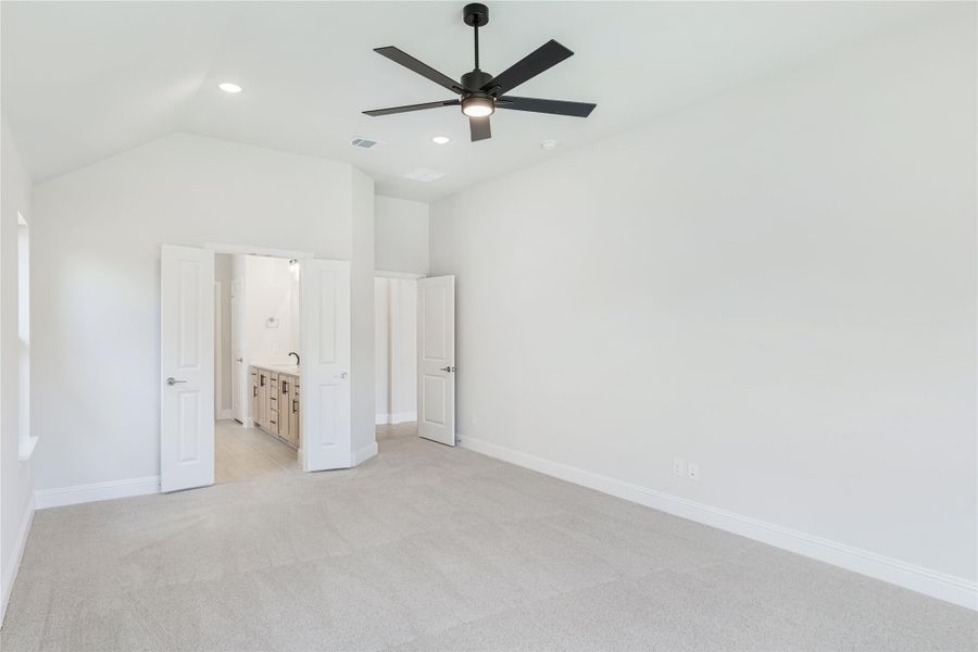 Empty bedroom with vaulted ceiling, black ceiling fan, carpet floors, and ensuite bathroom visible through open door.