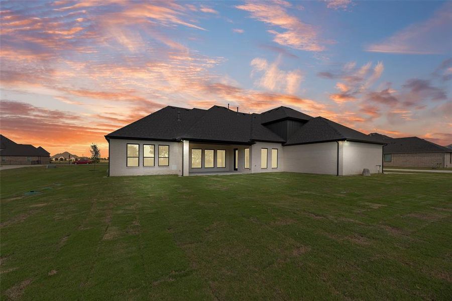 Rear view of house featuring a patio area, a lawn, and a shingled roof