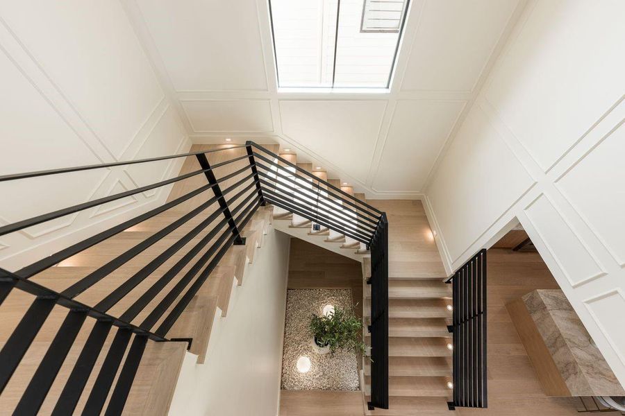 Viewed from the upper level, the stairwell becomes a design feature in its own right—clean lines intersecting with soft panel molding and layered illumination. At its core, a thoughtfully placed indoor planting bed introduces a calming, nature-infused counterpoint to the home’s tailored structure.