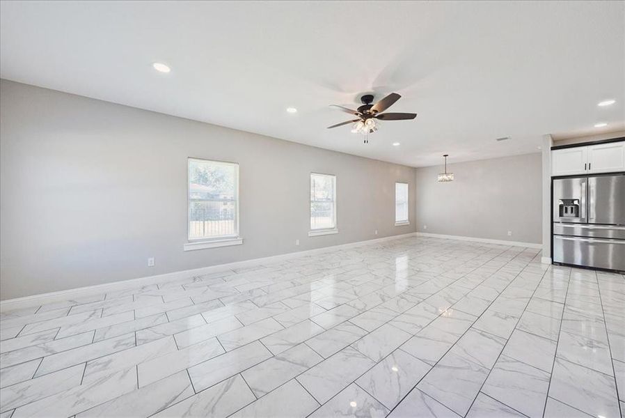 Unfurnished living room with recessed lighting, light marble finish flooring, ceiling fan, and a chandelier
