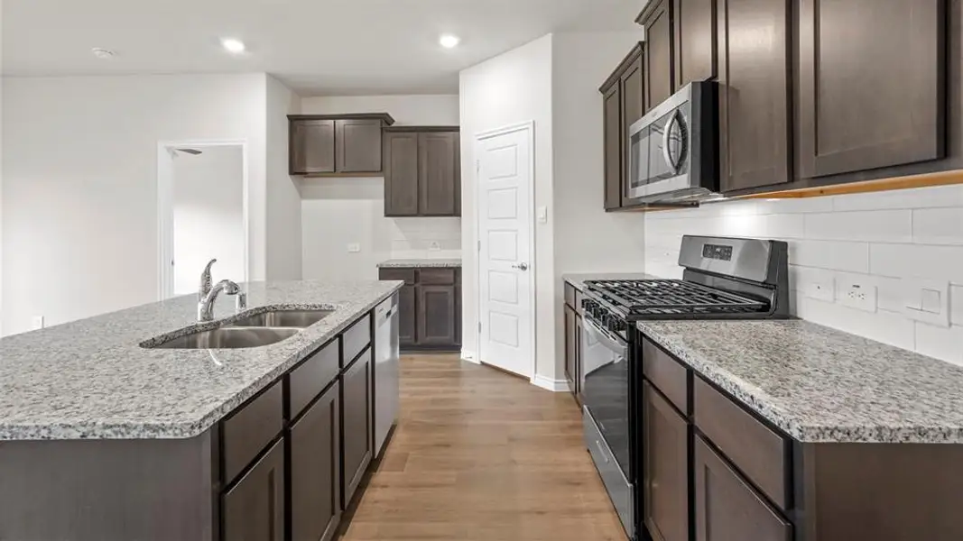 Contemporary kitchen featuring an island with a double basin sink, stone countertops, dark wood-finish cabinetry, stainless steel appliances, and wood-finish flooring
