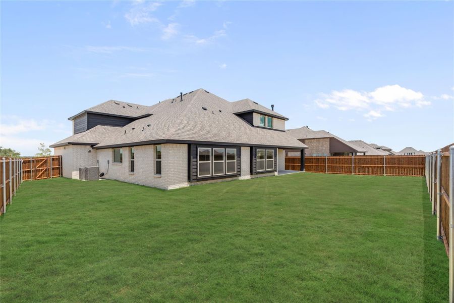 Rear view of brick home with large fenced backyard, green lawn, and covered patio area Rear view of brick home with large fenced backyard, green lawn, and covered patio area