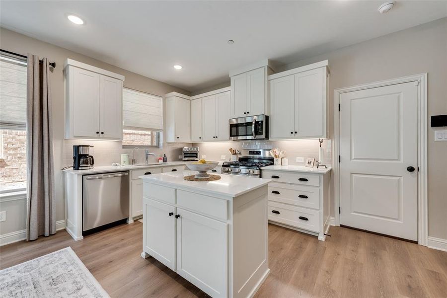 Kitchen featuring a central island with countertop, white cabinetry with black hardware, stainless steel appliances, upgraded Pergo water tight laminate wood look flooring, and recessed lighting Kitchen featuring a central island with countertop, white cabinetry with black hardware, stainless steel appliances, upgraded Pergo water tight laminate wood look flooring, and recessed lighting