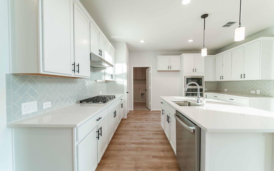 Kitchen featuring backsplash, light stone countertops, an island with sink, stainless steel appliances, and white cabinets