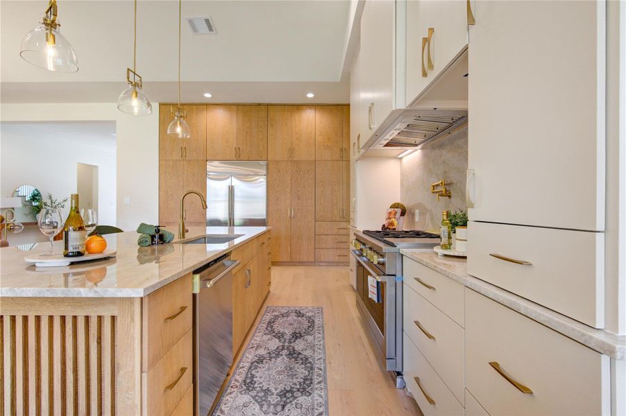 Designed for culinary enthusiasts and entertainers alike, the kitchen features a professional-grade gas range, statement stone backsplash, pot filler, premium stainless appliances, designer pendant lighting, and expansive prep surfaces. The seamless integration of the kitchen with the dining and living areas creates an ideal environment for hosting, allowing the chef to remain connected to the conversation while preparing meals.