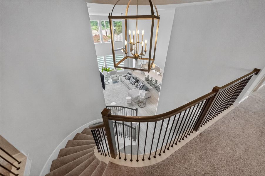 Elegant, curved staircase with wrought iron balusters overlooks the grand two-story living room, anchored by a striking chandelier and abundant natural light.