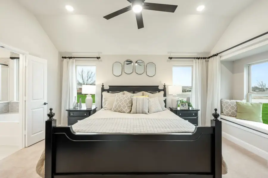 Master bedroom with black four-poster bed, ceiling fan, window seat, and ensuite bathroom door