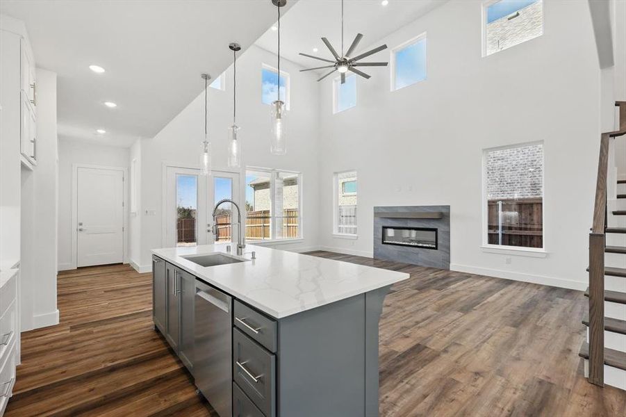 Kitchen featuring light stone counters, gray cabinetry, a sink, hanging light fixtures, and dishwasher