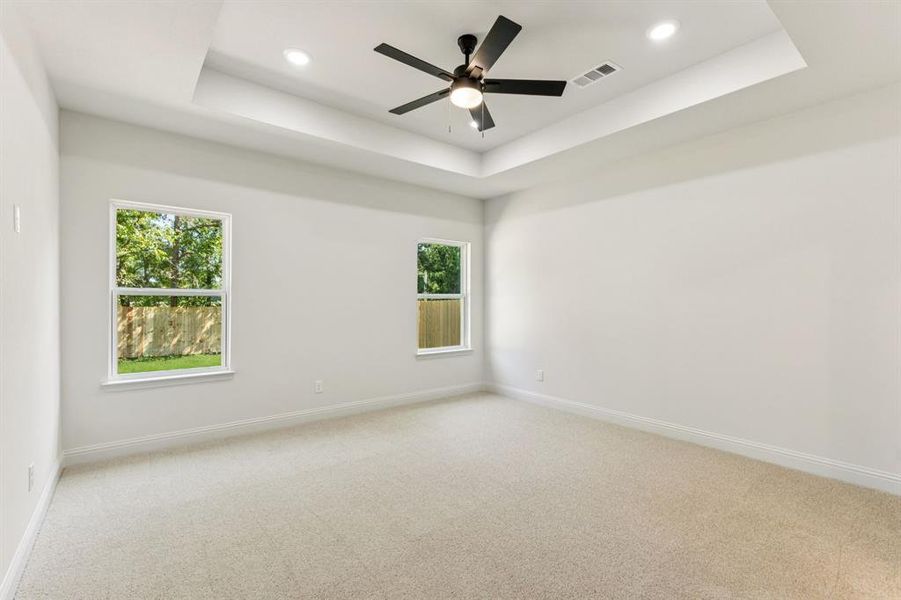 Empty room with a tray ceiling, carpet floors, healthy amount of natural light, ceiling fan, and recessed lighting