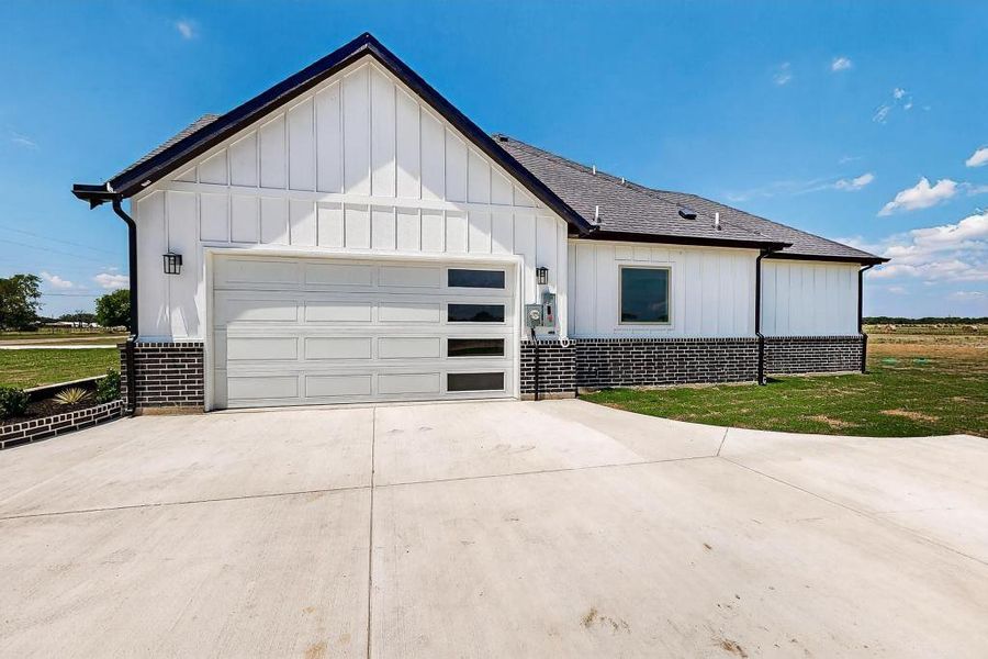 Modern inspired farmhouse with board and batten siding, concrete driveway, an attached garage, and brick siding