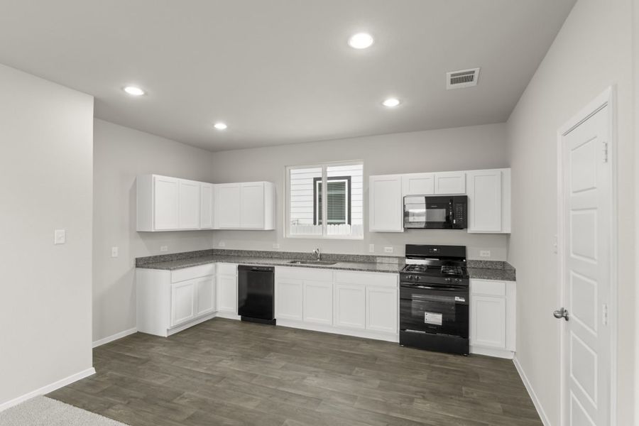 Image of a kitchen with white cabinets, brown vinyl flooring, granite countertops, black appliances and a window above the sink