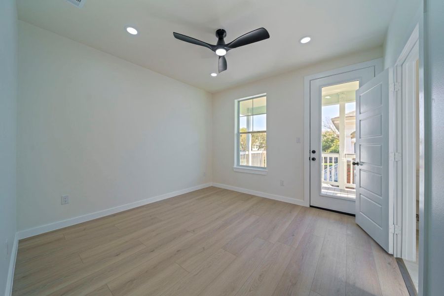 This bright primary room features light flooring, a ceiling fan, recessed lighting, a large window, and a door leading to a balcony with a pleasant view. This bright primary room features light flooring, a ceiling fan, recessed lighting, a large window, and a door leading to a balcony with a pleasant view.