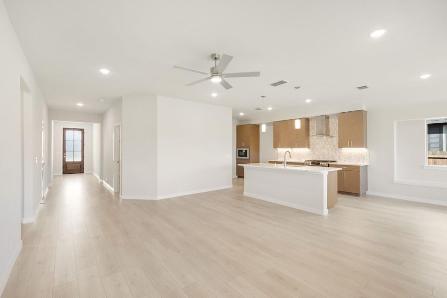 Open-concept living area and kitchen with white island, tan cabinets, light wood floors, and ceiling fan