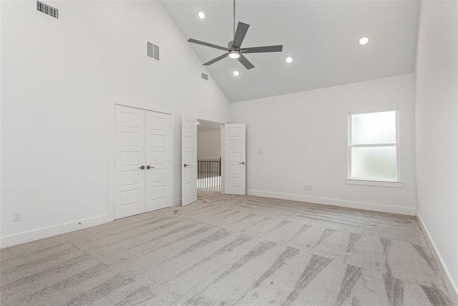 Unfurnished bedroom featuring ceiling fan, high vaulted ceiling, and light colored carpet