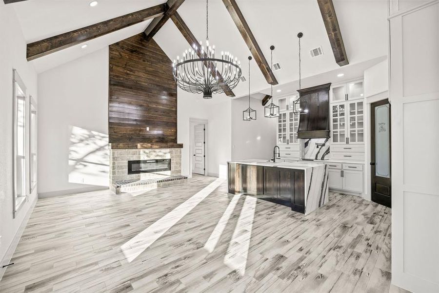 Kitchen with glass insert cabinets, high vaulted ceiling, decorative light fixtures, a center island with sink, and a brick fireplace Kitchen with glass insert cabinets, high vaulted ceiling, decorative light fixtures, a center island with sink, and a brick fireplace
