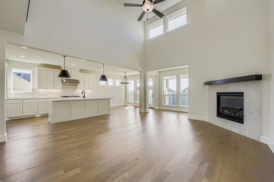 Unfurnished living room with light wood-type flooring, a tiled fireplace, a high ceiling, a chandelier, and ceiling fan