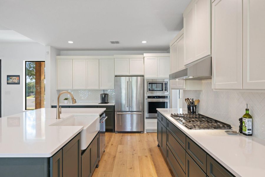 Kitchen featuring stainless steel appliances, white cabinetry, decorative backsplash, light wood-style flooring, and recessed lighting