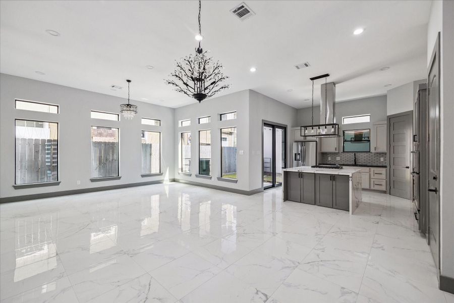 Seamless connection between the kitchen, dining, and living areas comes into full view. Windows line the walls, flooding the room with natural light and highlighting the polished tile floors.