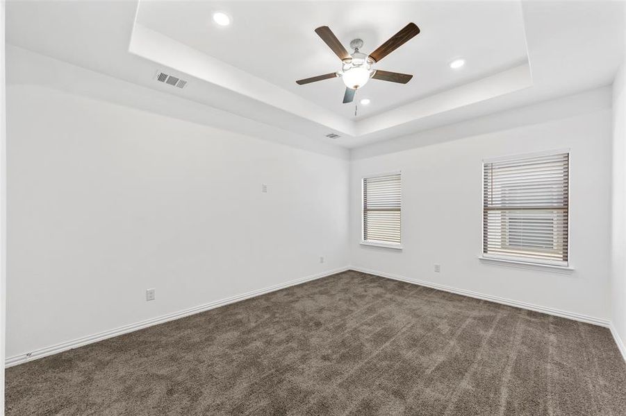 Unfurnished room with ceiling fan, a raised ceiling, and dark carpet