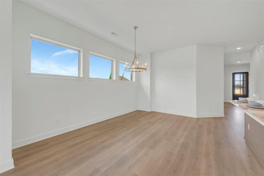Spacious dining area featuring wood-finish flooring, a contemporary chandelier, multiple rectangular windows, white walls, and white trim