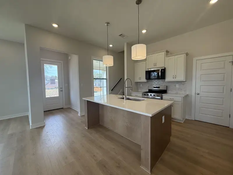 Two tone kitchen with stainless steel appliances, a center island with sink, tasteful backsplash, pendant lighting, and light stone countertops