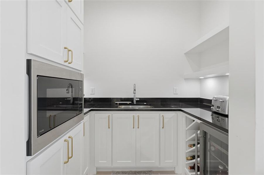 Compact kitchen area featuring white cabinetry with gold-toned hardware, dark countertops, and a stainless steel built-in microwave