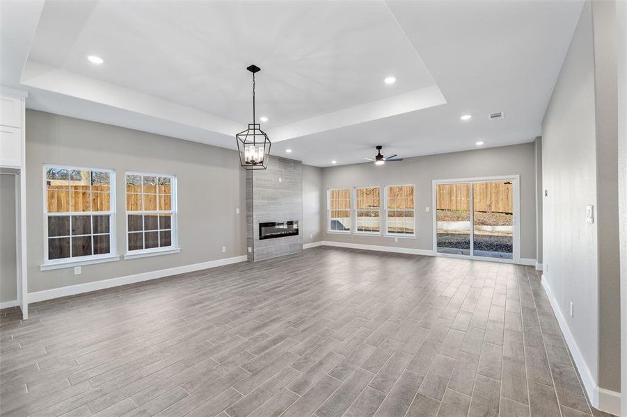 Unfurnished living room with a tray ceiling, ceiling fan with notable chandelier, a tile fireplace, and light hardwood / wood-style floors