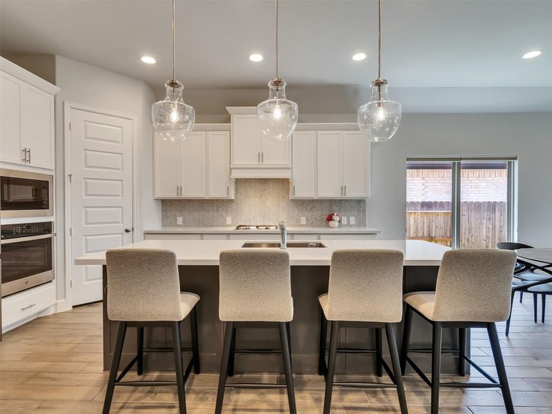 Modern kitchen featuring a spacious island with elegant pendant lighting, sleek cabinetry, and a built-in oven, offering a perfect blend of style and functionality.