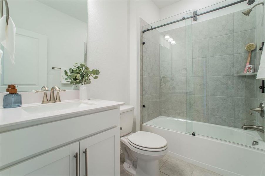 Full bathroom featuring shower / bath combination with glass door, vanity, and light tile patterned floors Full bathroom featuring shower / bath combination with glass door, vanity, and light tile patterned floors