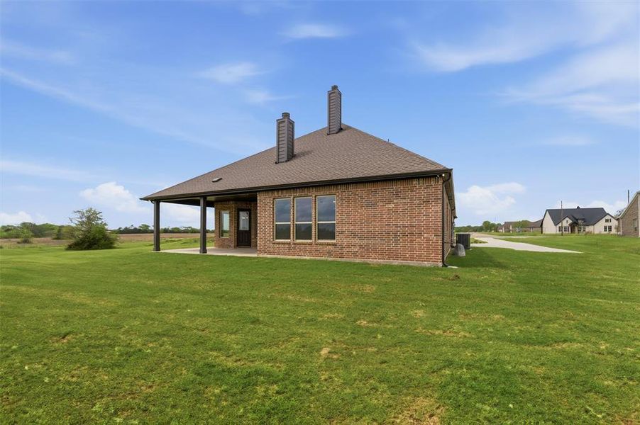 Back of house featuring a chimney, a yard, a patio area, brick siding, and roof with shingles