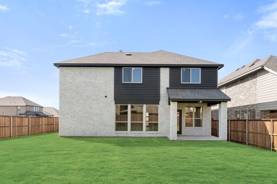 Two-story home rear view with light brick, dark siding, covered patio, and fenced backyard with green lawn