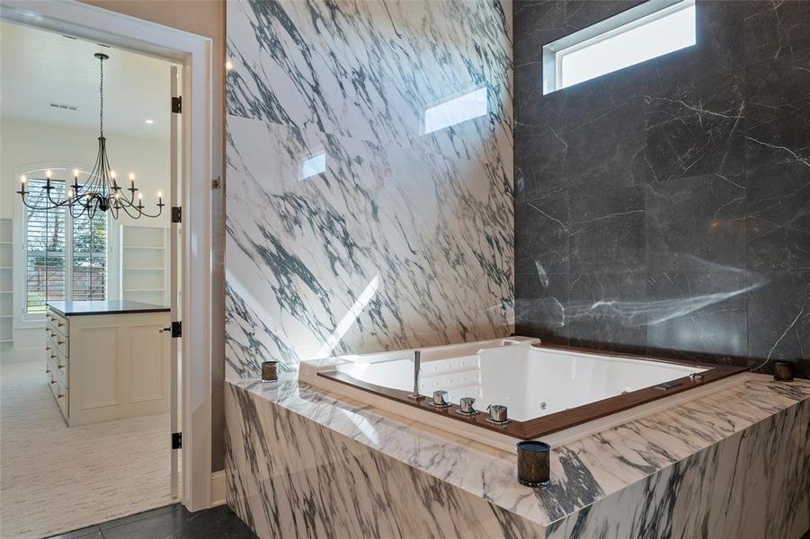 Bathroom with a jetted tub, a chandelier, tile walls, and dark tile patterned floors