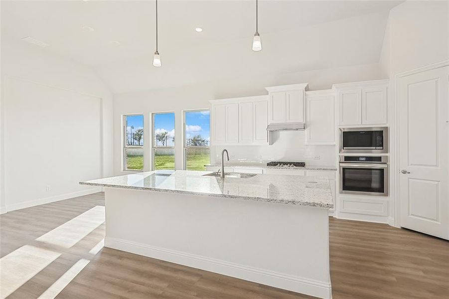 Kitchen with sink, vaulted ceiling, decorative light fixtures, white cabinetry, and appliances with stainless steel finishes