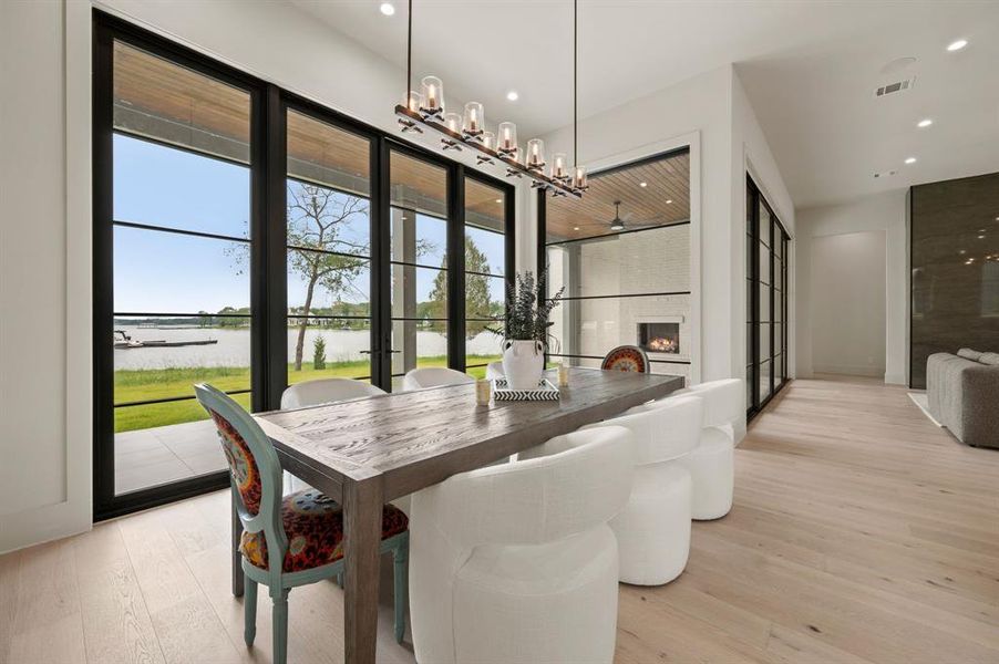 Dining area featuring a water view, a chandelier, light wood-type flooring, recessed lighting, and a fireplace Dining area featuring a water view, a chandelier, light wood-type flooring, recessed lighting, and a fireplace