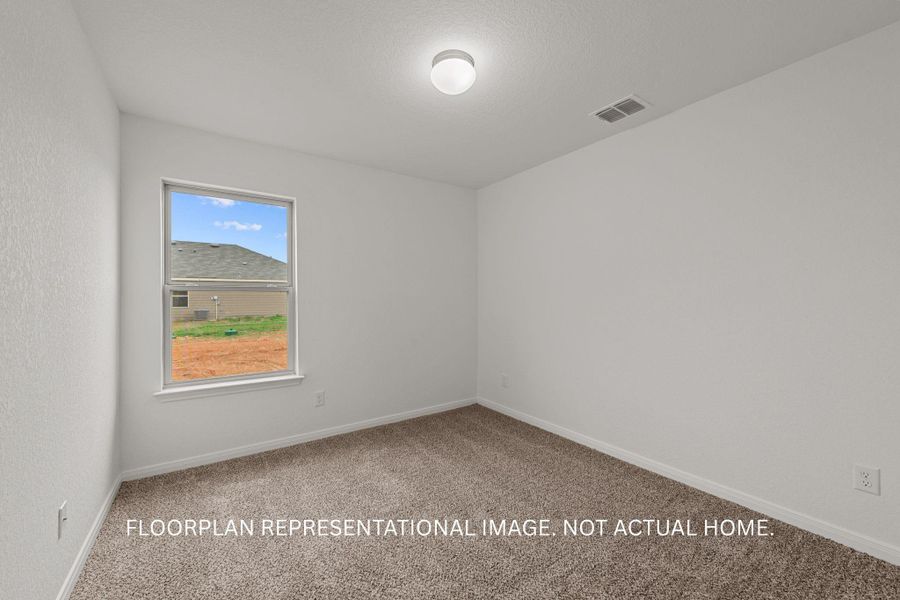 A well-lit bedroom features plush carpet and a window overlooking a developing neighborhood.
