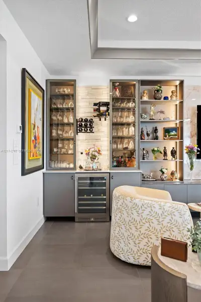 Built-in wet bar featuring custom cabinetry, integrated wine refrigerator, recessed display shelving with internal lighting, and a textured stone backsplash