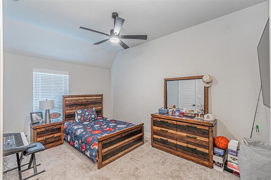 Carpeted bedroom featuring a vaulted ceiling with a ceiling fan, a window with horizontal blinds, and light-toned walls