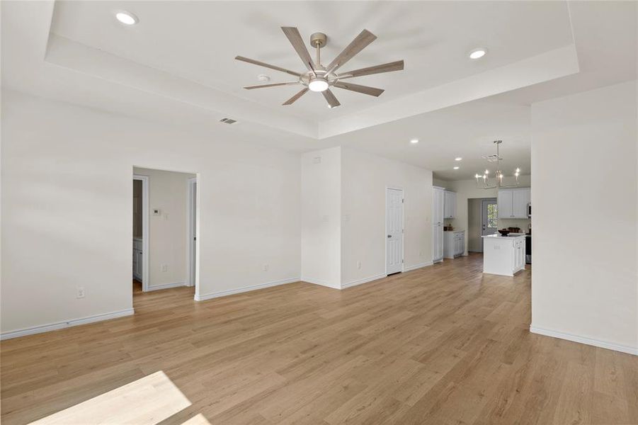 Unfurnished living room with a raised ceiling, recessed lighting, light wood-style floors, a chandelier, and a ceiling fan Unfurnished living room with a raised ceiling, recessed lighting, light wood-style floors, a chandelier, and a ceiling fan