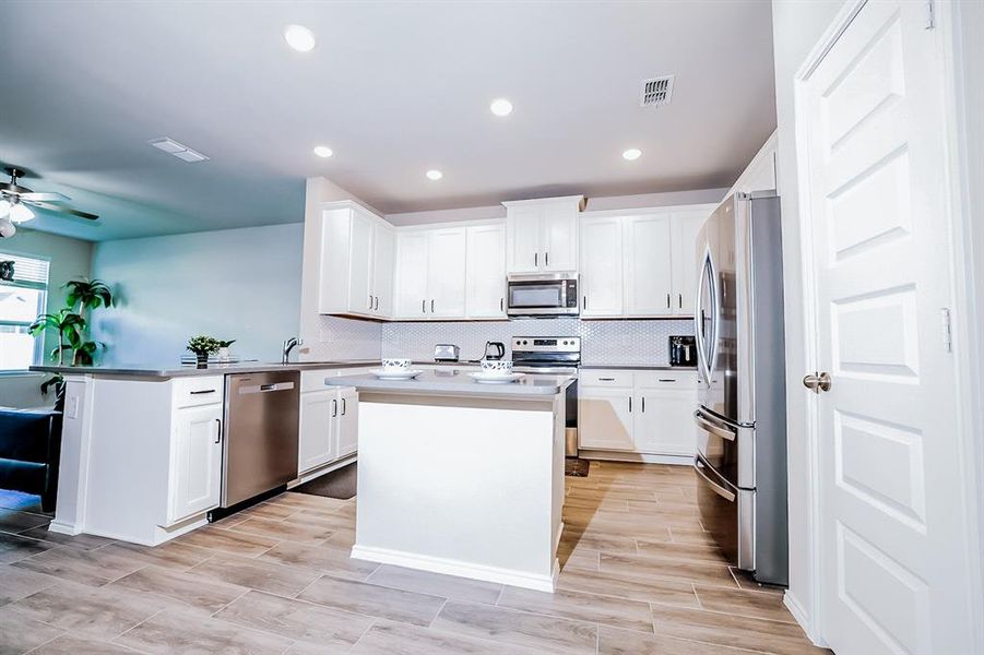 Kitchen with white cabinets, decorative backsplash, a kitchen island, and stainless steel appliances