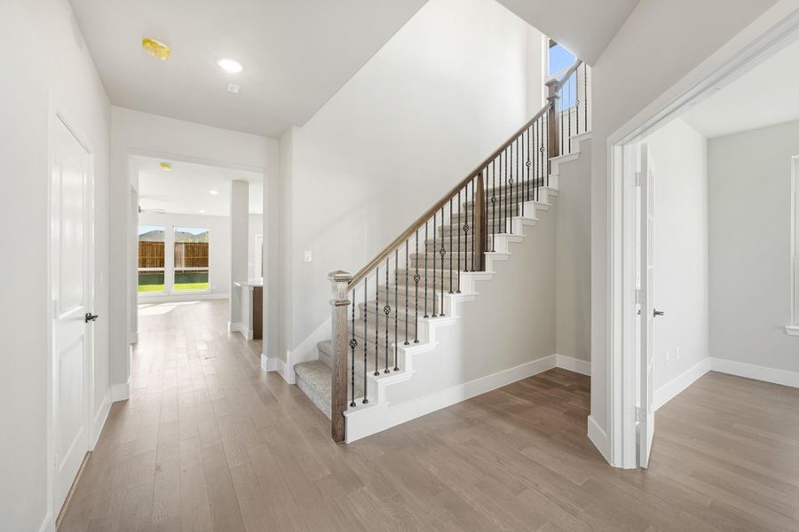 Bright entryway with wood and iron staircase, hardwood floors, and white walls leading to main living area.