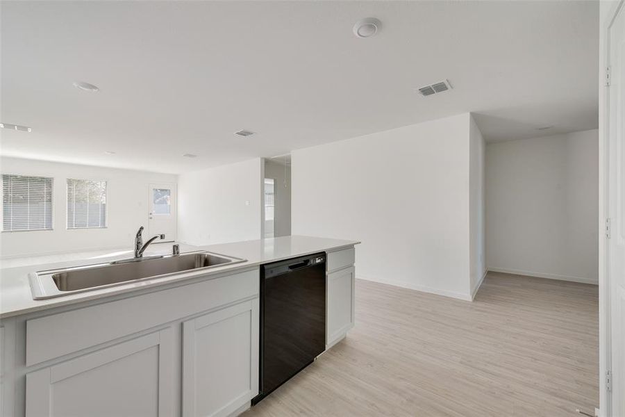 Kitchen with black dishwasher, light hardwood / wood-style flooring, white cabinets, and sink