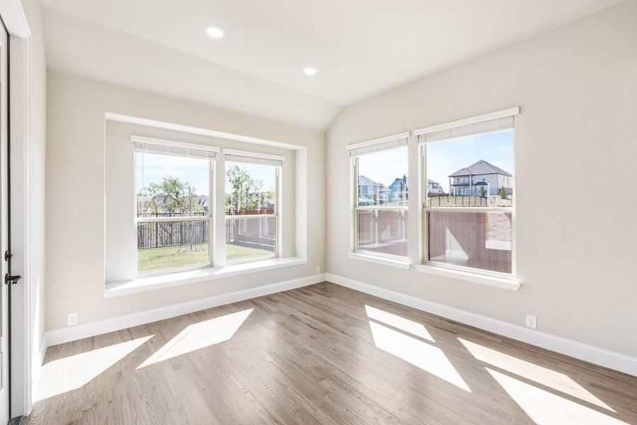 Empty room with hardwood floors, white walls, and large windows overlooking a backyard