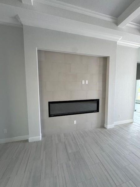 Detailed view of a tiled fireplace, ornamental molding, wood finish floors, and a textured ceiling