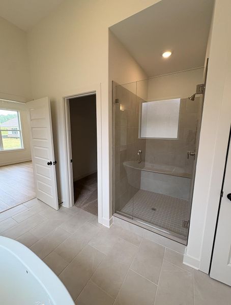 Spacious bathroom featuring a glass-enclosed shower with bench seating, a freestanding tub, and large format tile flooring